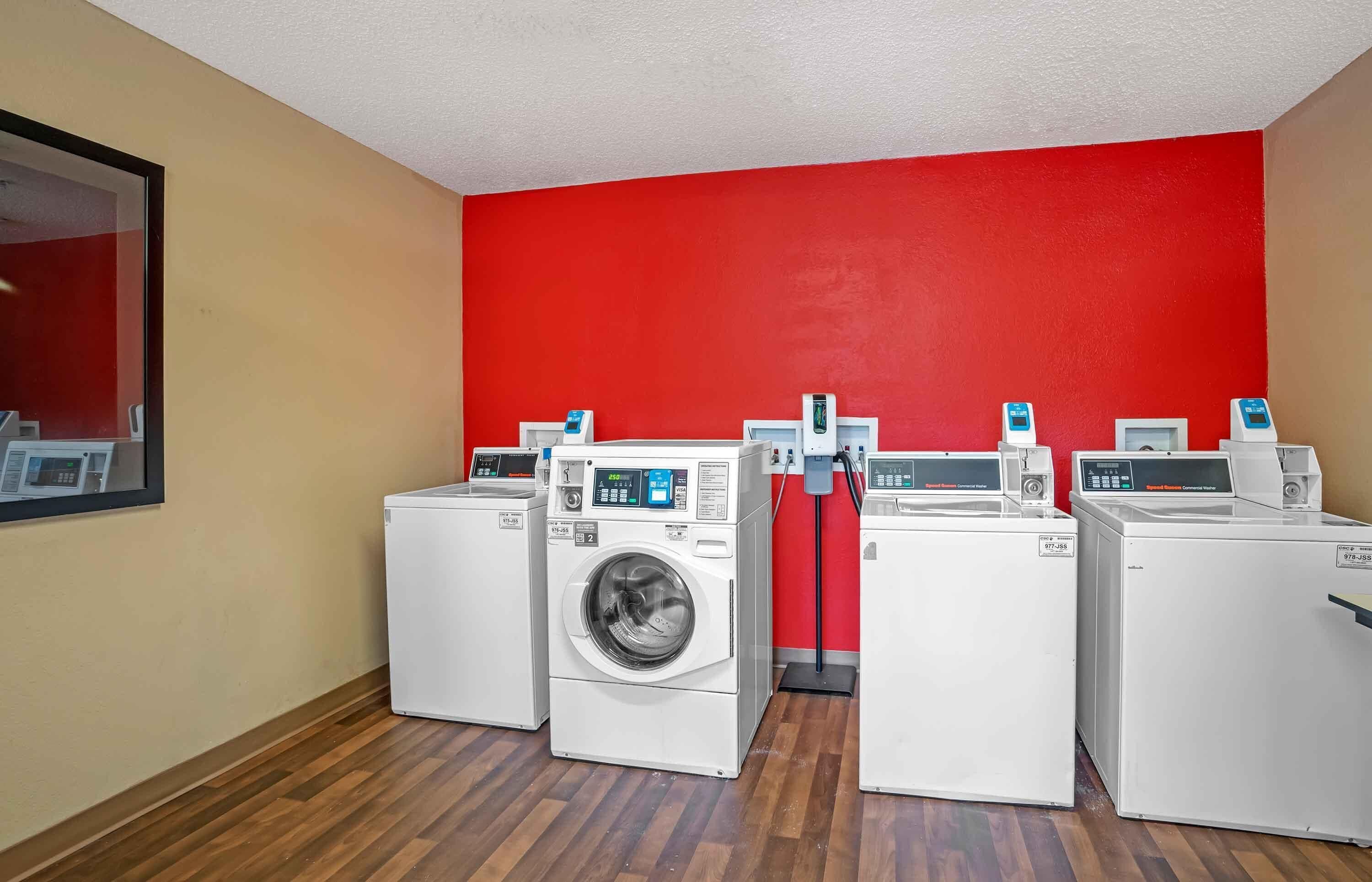 A laundry room with four washing machines, a red wall, and wooden flooring.
