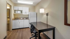 A compact kitchen with white cabinets, a microwave, and a refrigerator. There's a small dining table with a chair. - Extended Stay America Suites Chesapeake Crossways Blvd (Chesapeake)