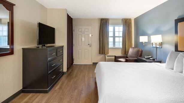 A hotel room with a bed, a TV on a dresser, a desk with a chair, and a window with curtains. - Extended Stay America Suites Chesapeake Crossways Blvd (Chesapeake)