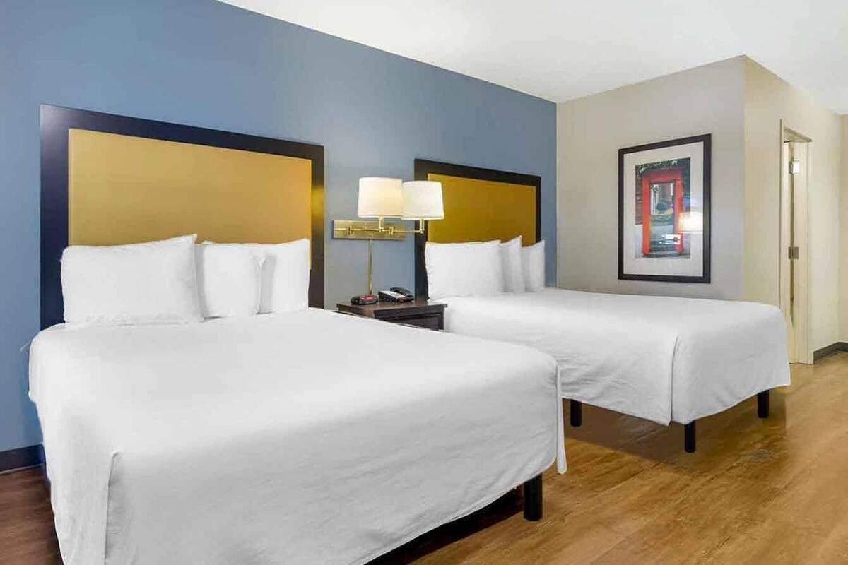 A hotel room with two beds, a nightstand with a lamp, and a framed picture on the wall.