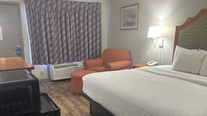 A hotel room with a bed, a desk with a computer, a chair, a lamp, and a window with curtains. - Days Inn by Wyndham Jacksonville (Jacksonville)