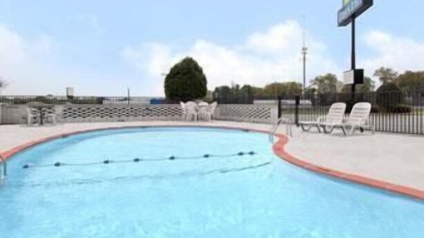 A swimming pool with a red edge, a fence, and a sign in the background. - Days Inn by Wyndham Jacksonville (Jacksonville)