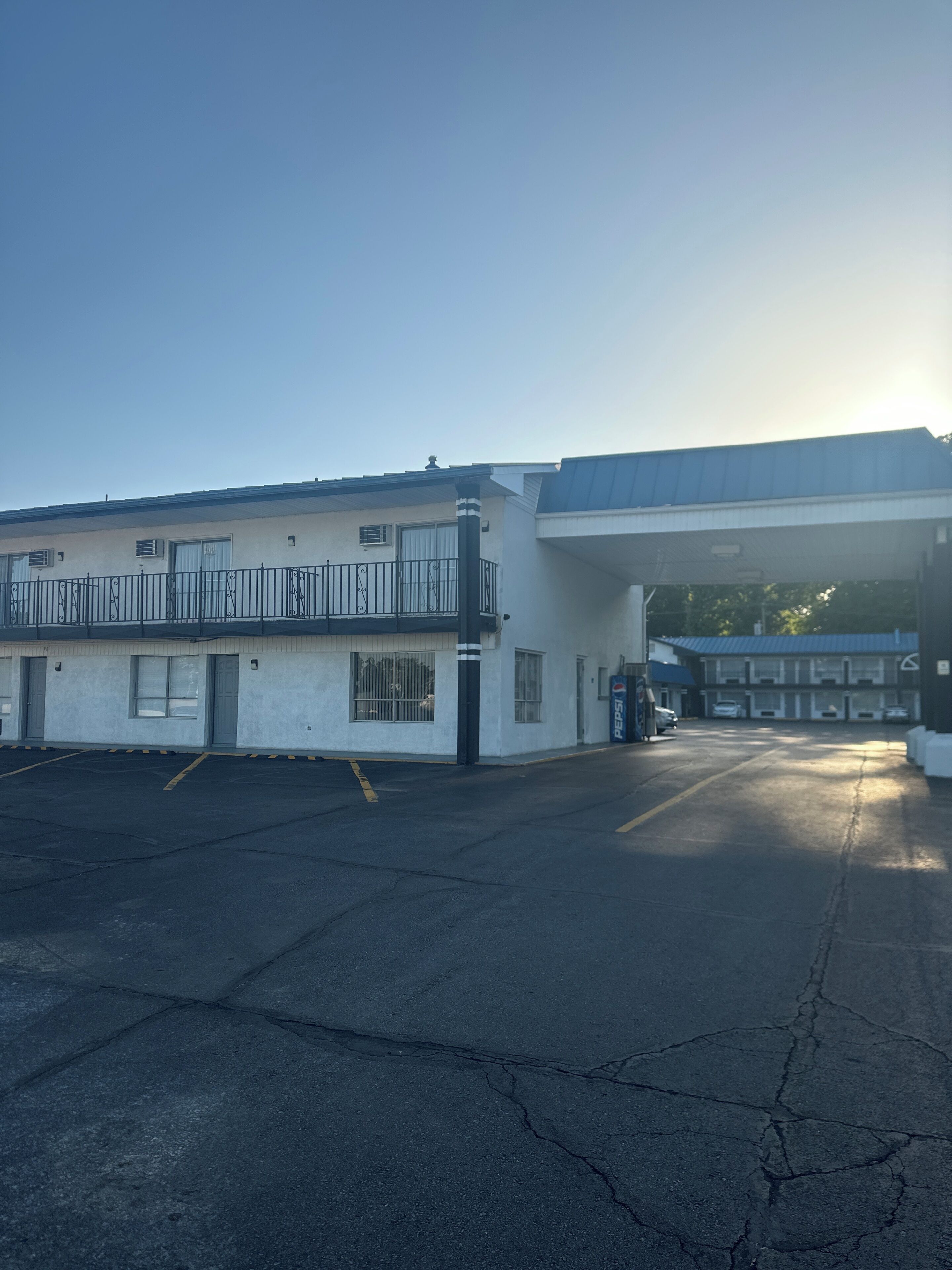 A parking lot with a building that has a flat roof, a covered area, and a Pepsi sign.
