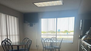 A room with a dining table and chairs, a TV mounted on the wall, and a window with blinds. - Days Inn by Wyndham Jacksonville (Jacksonville)