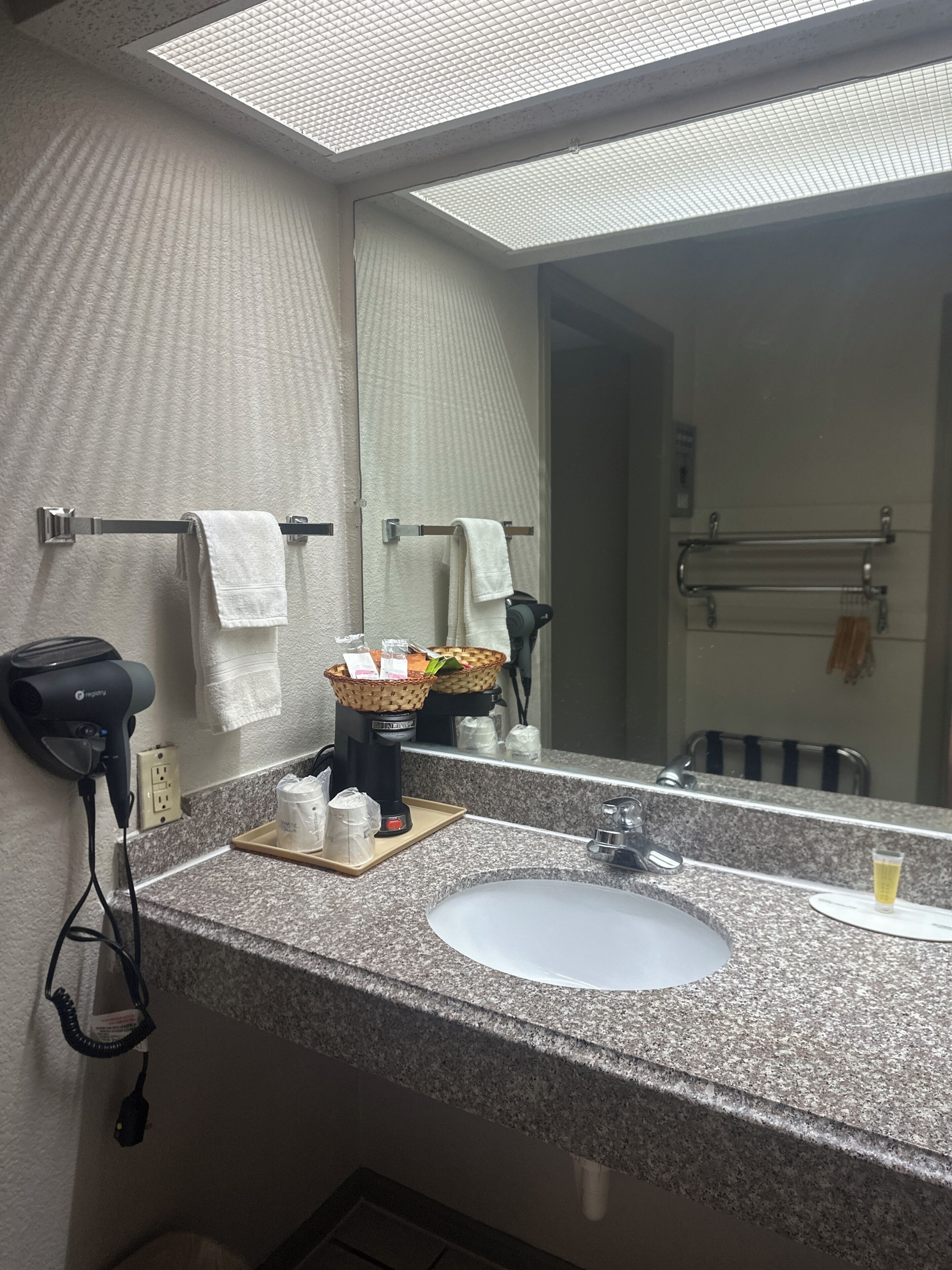 A bathroom with a granite countertop, a sink, a mirror, and a hairdryer on a wall socket.