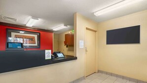 Zona de recepción con mostrador negro, un letrero que dice 'WELCOME', una pantalla digital y una puerta que da a una habitación.