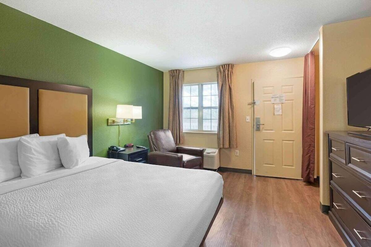 Una camera d'albergo con un letto grande, una scrivania con una lampada, una sedia, una televisione e una porta.