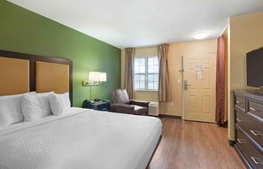 Relax in this serene space with a large bed against a calming backdrop, a comfortable chair, and a convenient table with a lamp.