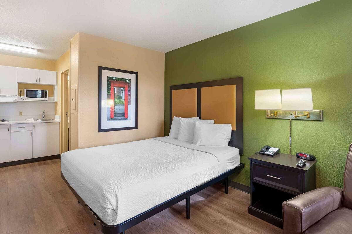 Una camera d'albergo con un letto, un comodino con una lampada, un telefono e una piccola credenza.