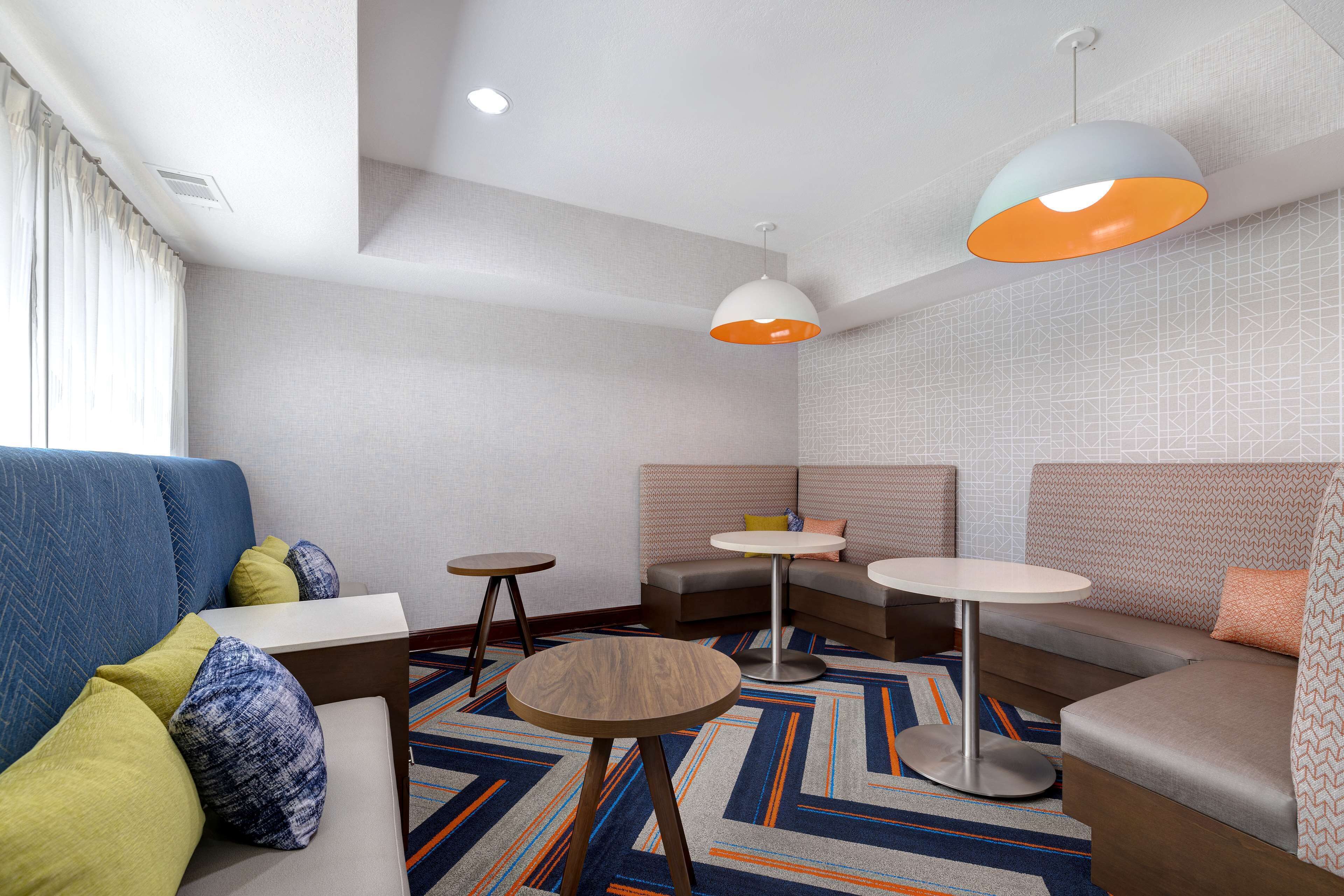A modern hotel room with a blue sofa, a brown sofa, a small round table, and two pendant lights.