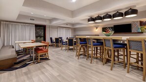 A modern dining area with a long wooden table, blue cushioned chairs, and a bar counter with stools. - Hampton Inn Hot Springs (Hot Springs)