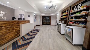 A hotel reception area with a wooden reception desk, a digital check-in station, a refrigerator with snacks, and a 'BAR' sign above a snack shelf. - Hampton Inn Hot Springs (Hot Springs)