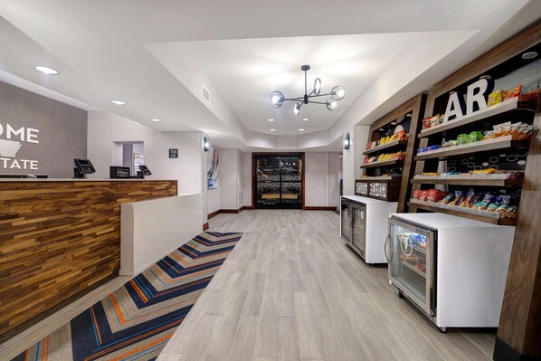 A hotel reception area with a wooden reception desk, a digital check-in station, a refrigerator with snacks, and a 'BAR' sign above a snack shelf. - Hampton Inn Hot Springs (Hot Springs)