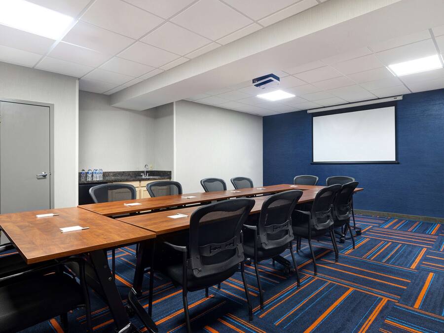 A conference room with a long table, chairs, a projector screen, and a carpeted floor.