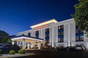 A Hampton Inn hotel with a modern facade, a covered entrance, and a parking lot with several cars.
