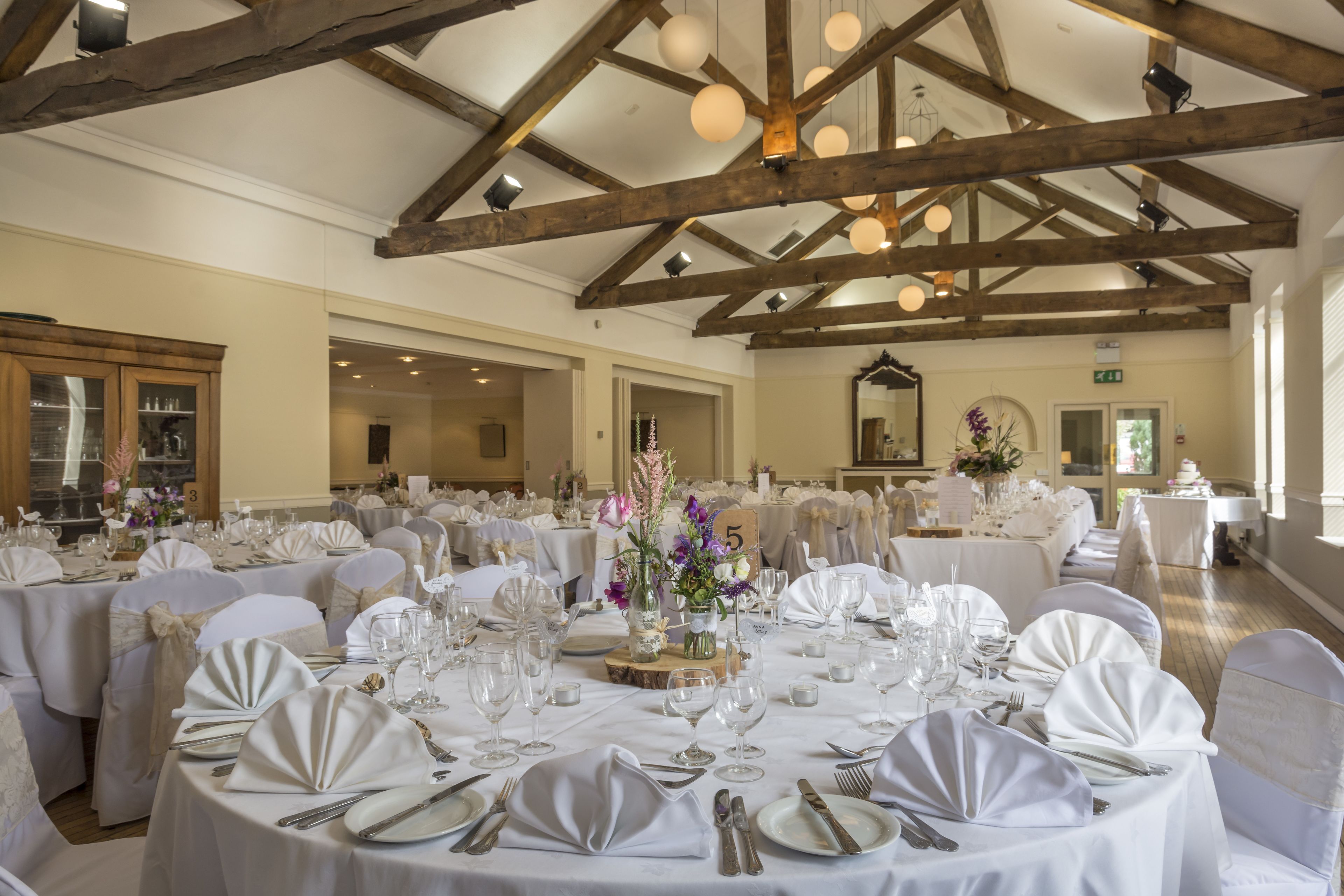 Un saló de banquets amb taules rodones preparades per a un esdeveniment formal, amb teles blanques, coberts i centrals florals.