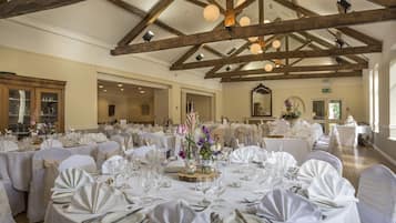 Un saló de banquets amb taules rodones preparades per a un esdeveniment formal, amb teles blanques, coberts i centrals florals.