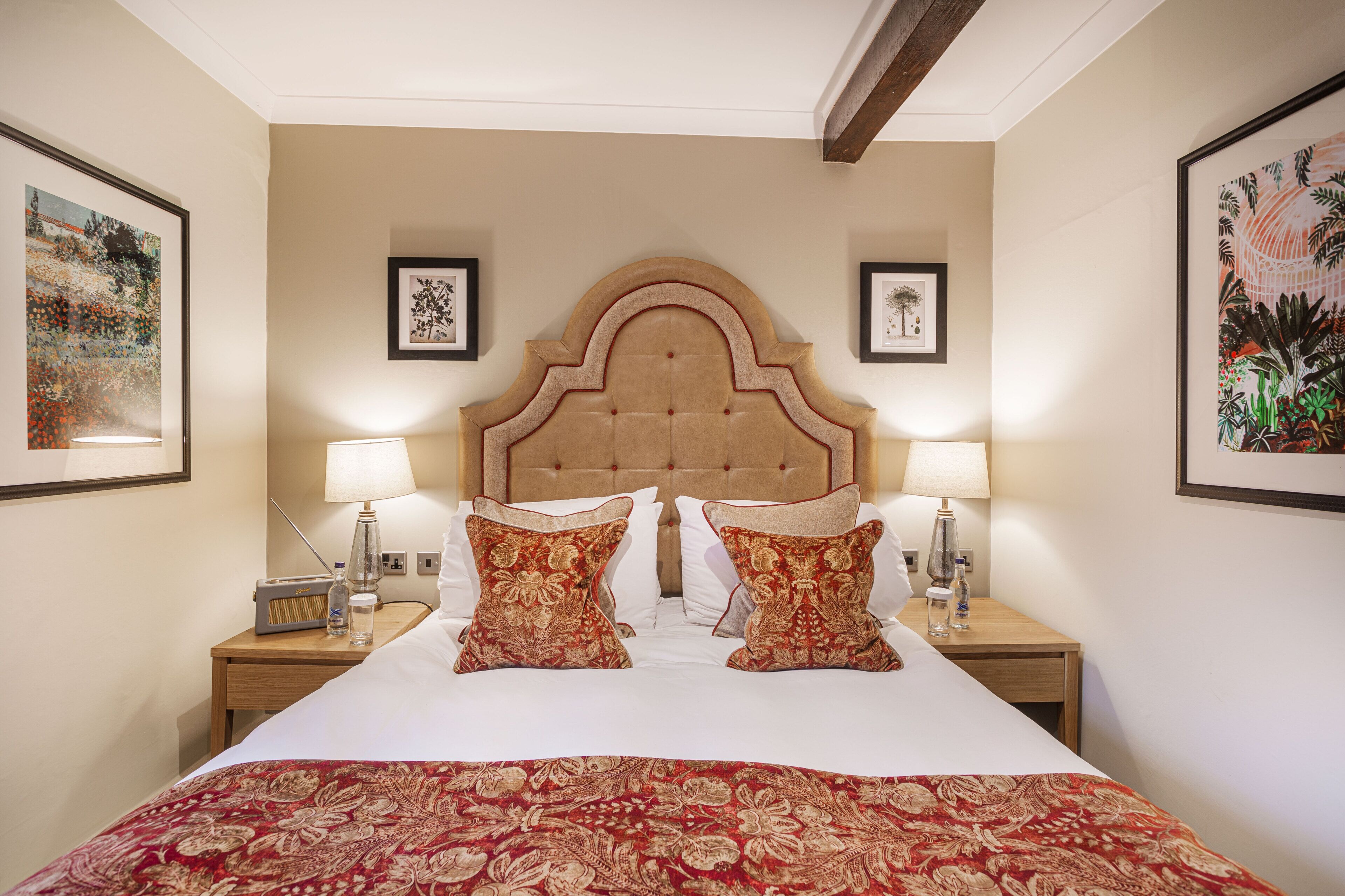 Quarto de hotel com uma cama grande, duas mesas de cabeceira com abajures e quadros nas paredes.