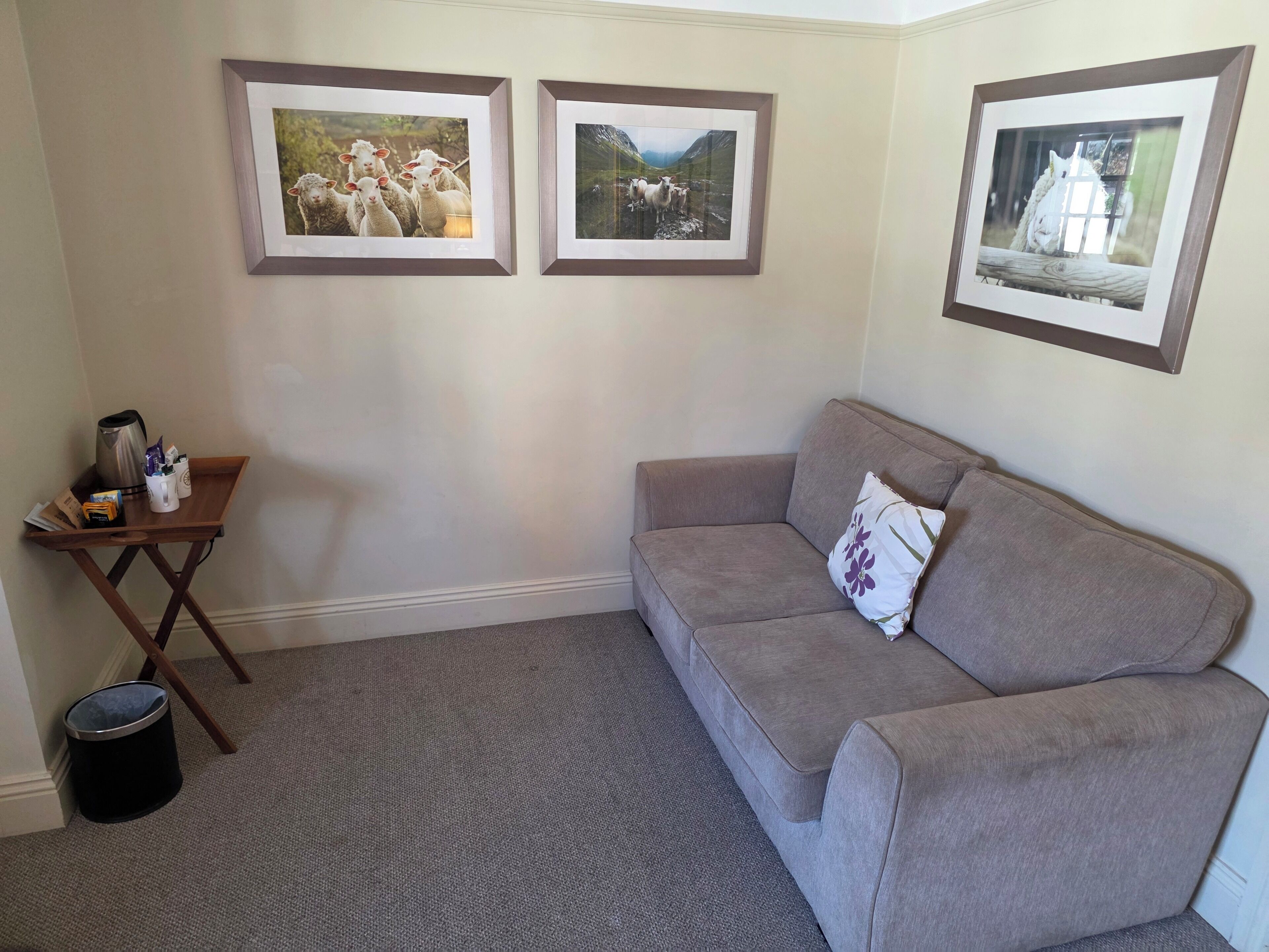 A living room with a grey sofa, a small wooden side table, and three framed pictures on the wall.