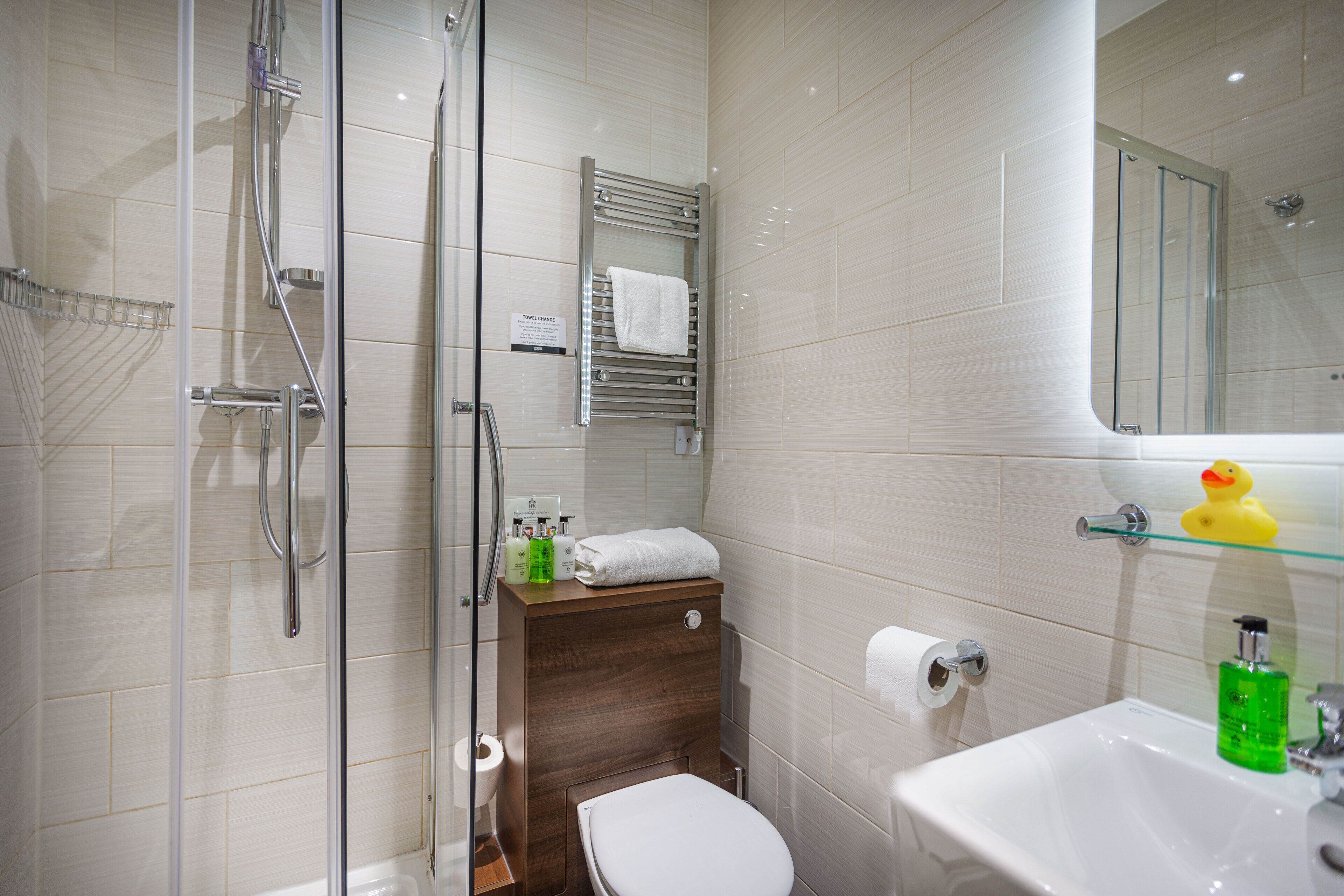 A modern bathroom with a glass shower enclosure, a wooden vanity, a white sink, and a yellow rubber duck on the shelf.