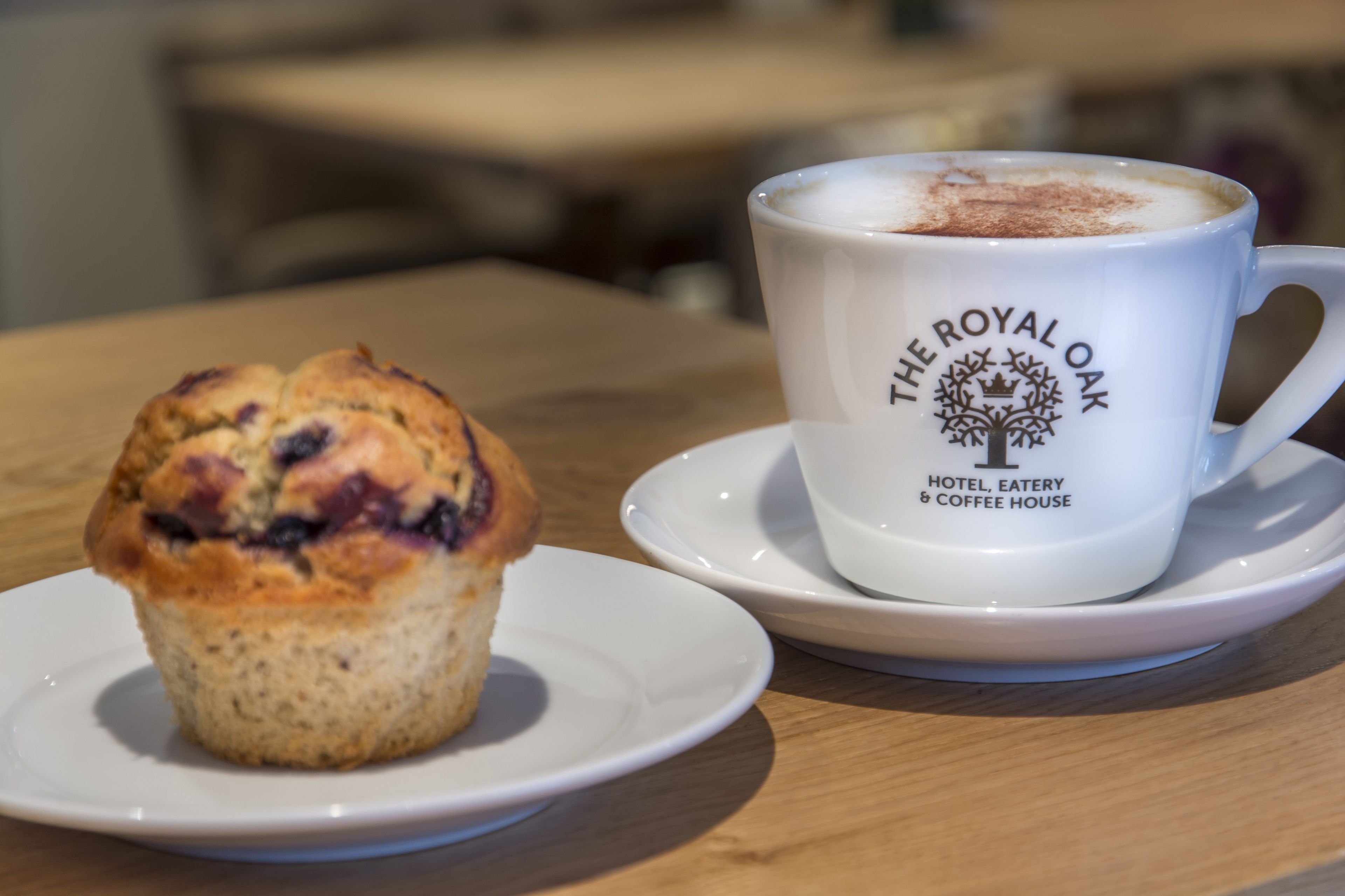 A muffin on a plate and a cup with "The Royal Oak Hotel, Eatery & Coffee House" logo.