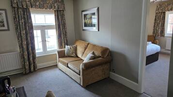 A room with a sofa, a radiator, a window with curtains, a framed picture on the wall, and a door leading to another room.