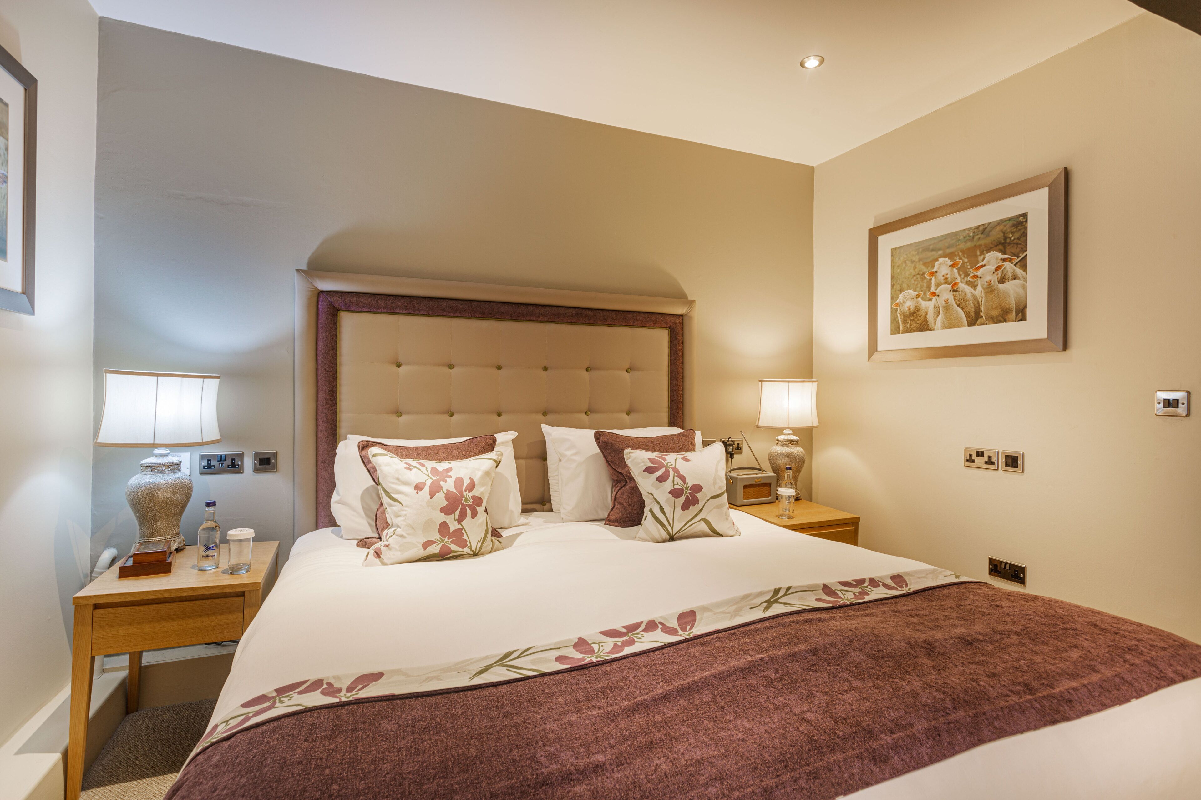 A hotel room with a large bed, two bedside tables, a nightstand, a lamp, a framed picture on the wall, and a carpeted floor.
