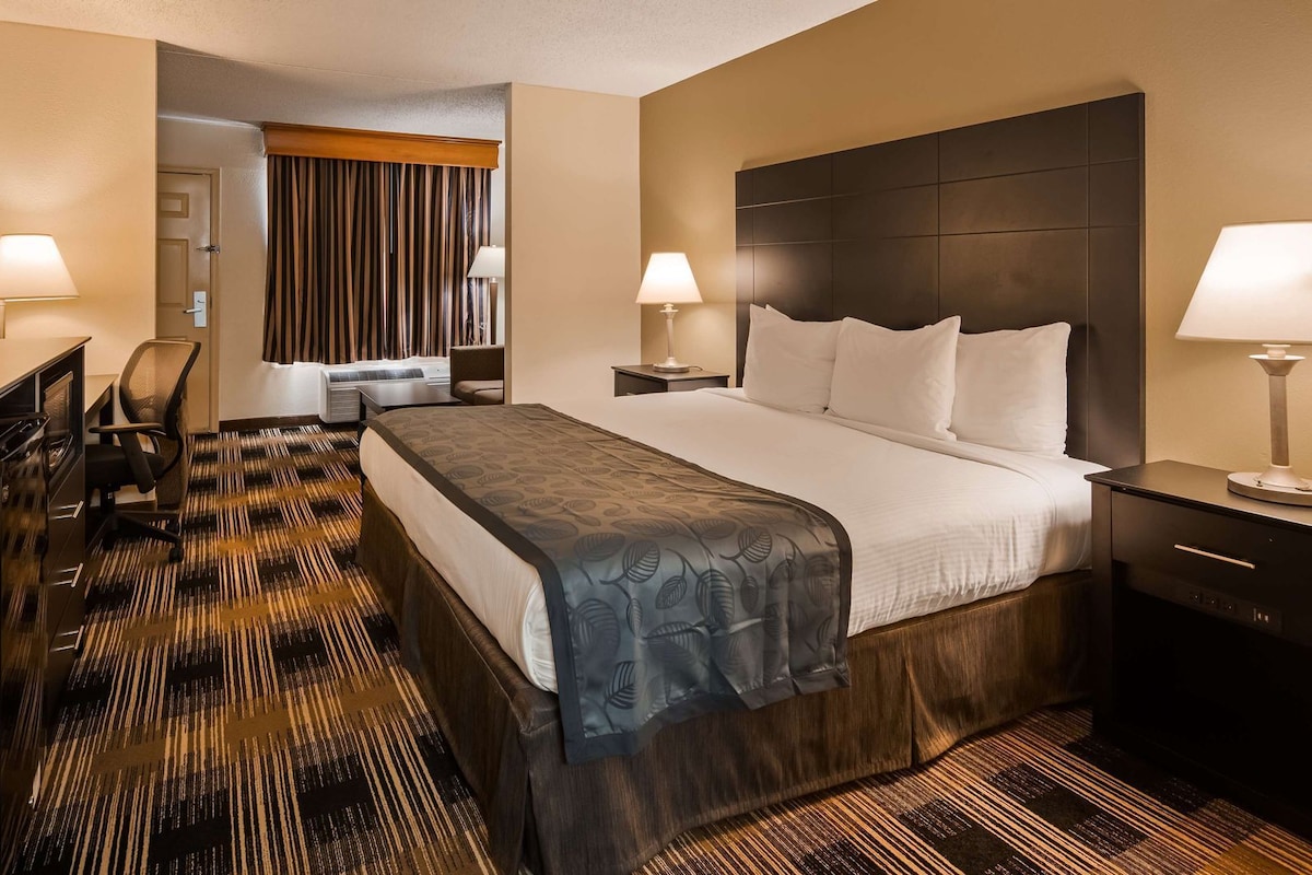 A hotel room with a large bed, two bedside tables with lamps, a desk with a computer, a chair, a wardrobe, and a television.