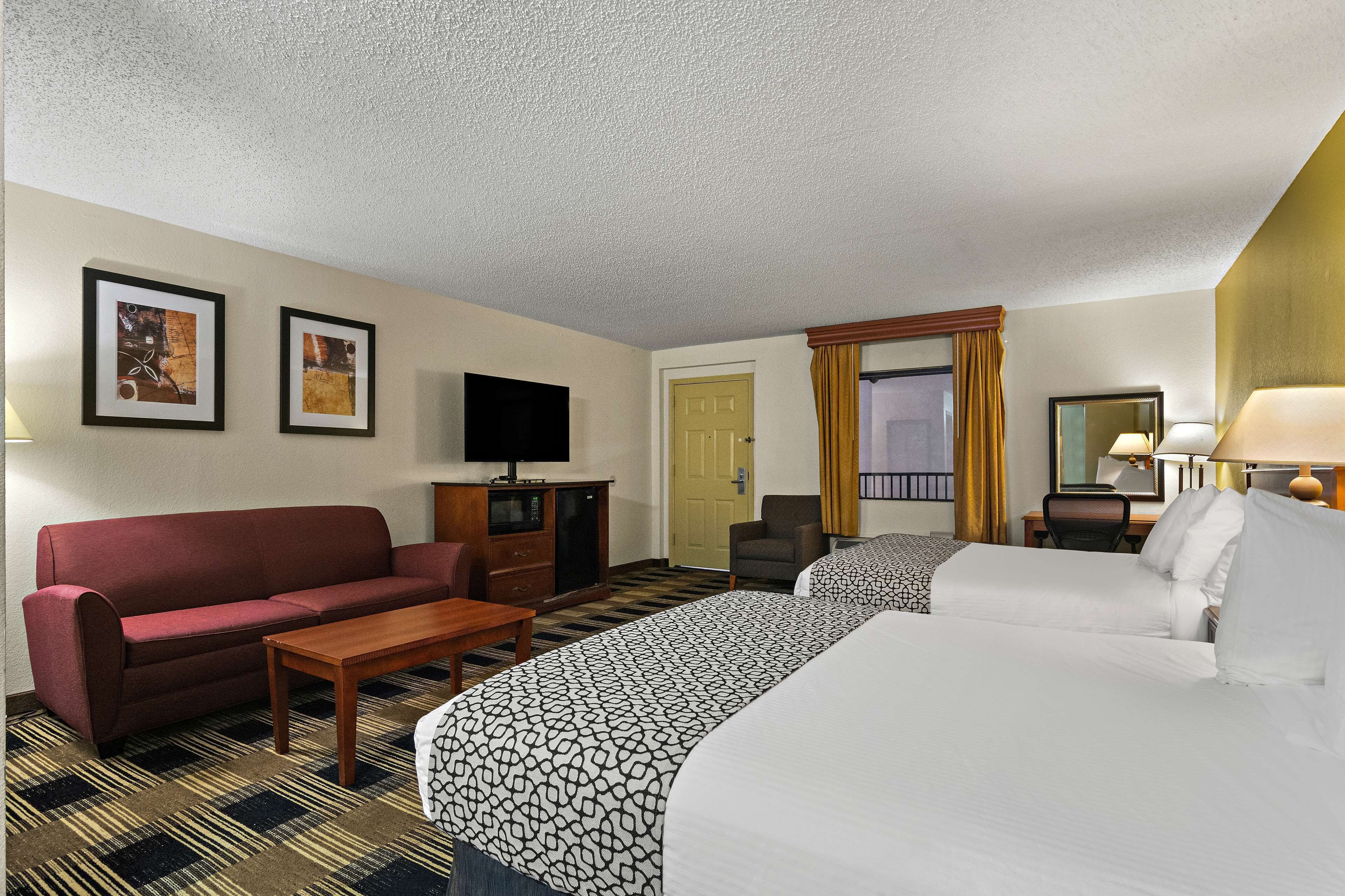 A hotel room with two beds, a sofa, a TV, a desk, and a chair.