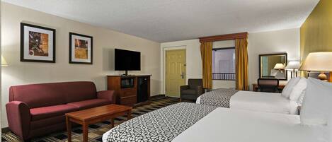 A hotel room with two beds, a sofa, a TV, a desk, and a chair.