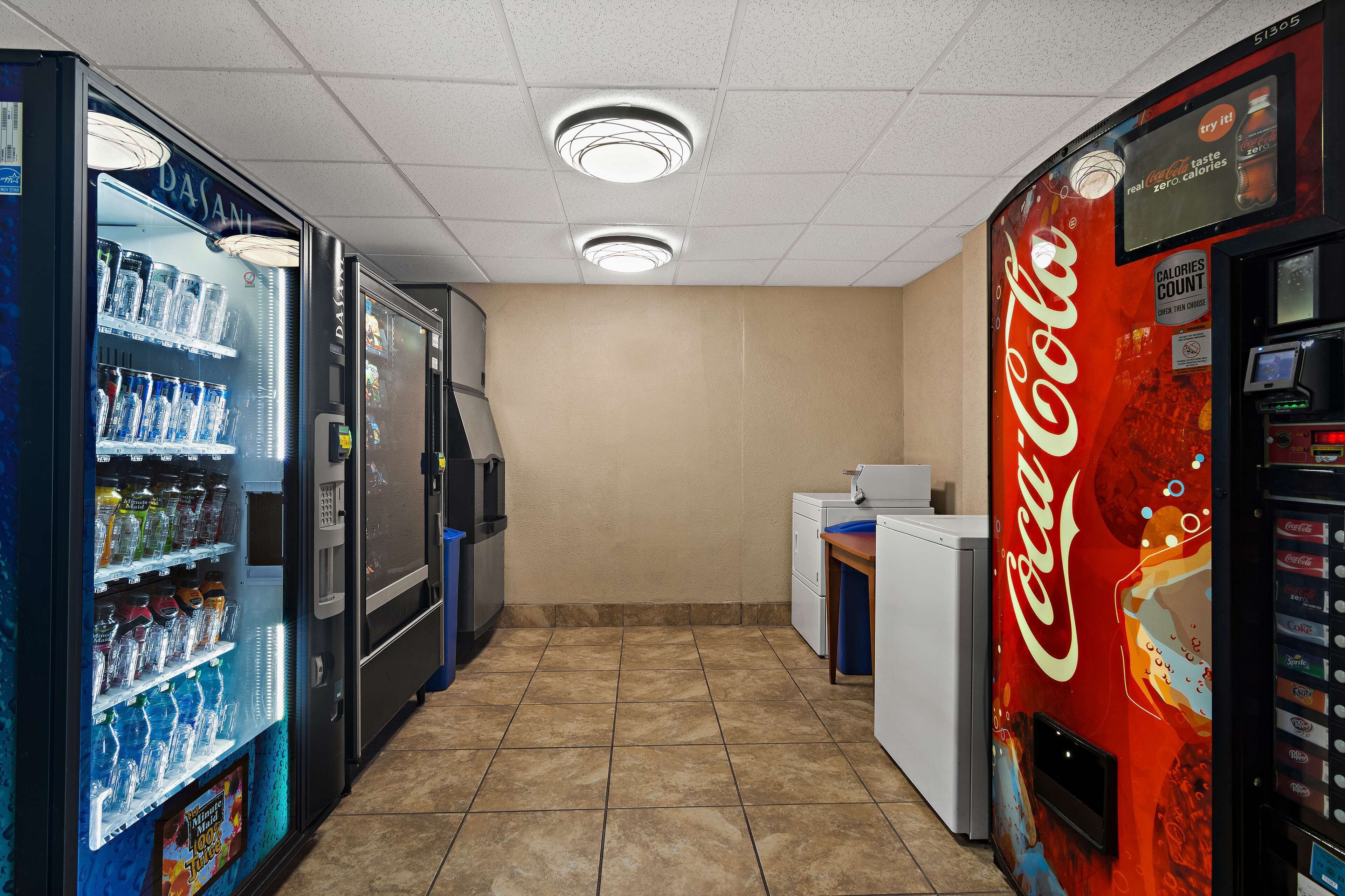 Zona de máquinas expendedoras con Dasani y Coca-Cola, un refrigerador y un cubo de basura.