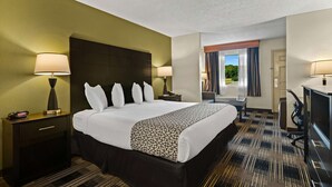 A hotel room with a large bed, two bedside tables with lamps, a desk with a chair, and a view of the outdoors through the window. - Best Western Windsor Suites (Fayetteville)