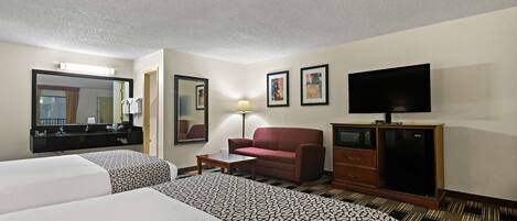 A hotel room with two beds, a sofa, a TV, a desk, and a mirror.
