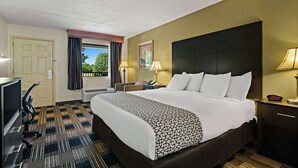 A hotel room with a large bed, a desk, a chair, a TV, and a window with curtains. - Best Western Windsor Suites (Fayetteville)