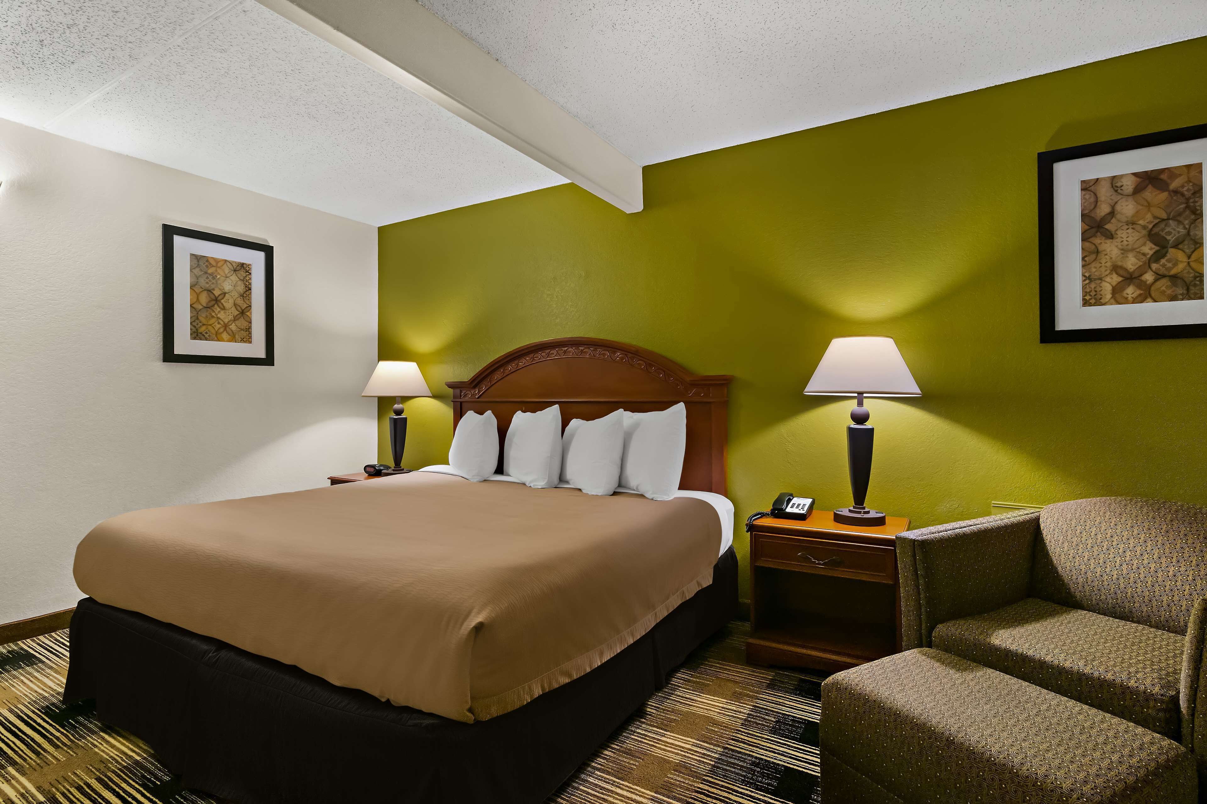 A hotel room with a large bed, two bedside lamps, a chair, and artwork on the walls.