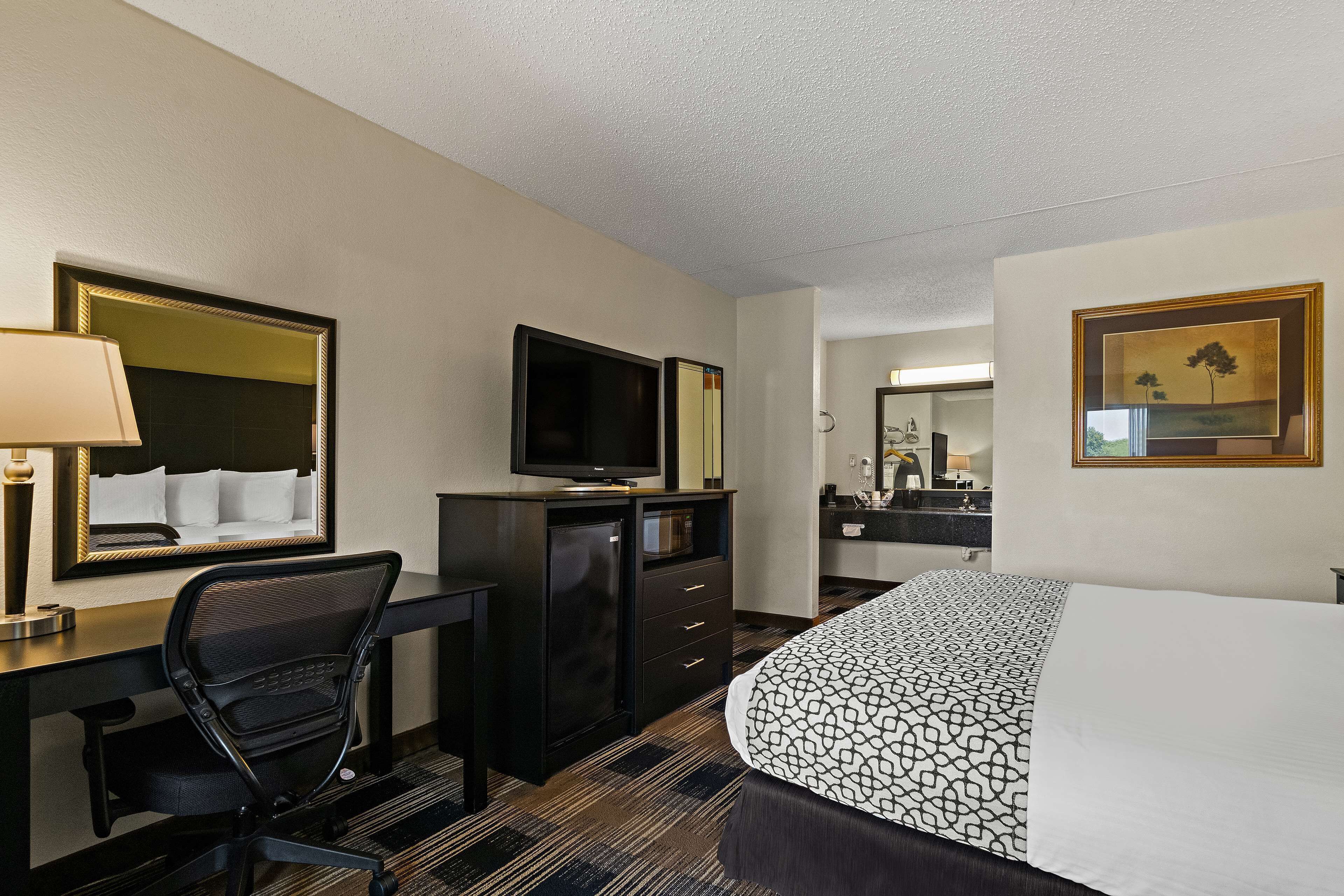 Una habitación de hotel con cama, escritorio, silla, televisión y cómoda.