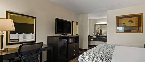 Una habitación de hotel con cama, escritorio, silla, televisión y cómoda.