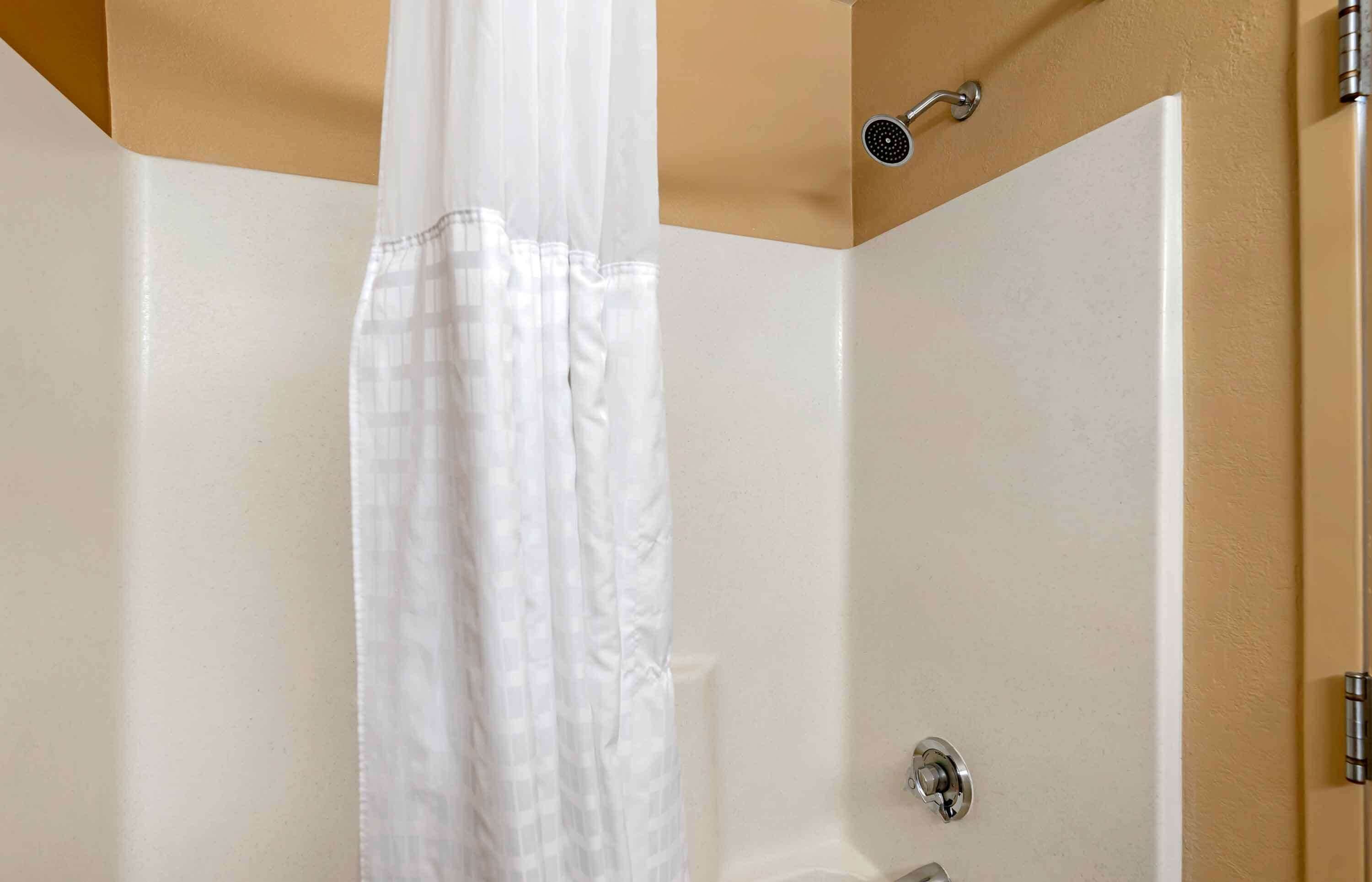 A shower with a white curtain, a handheld showerhead, and a door with a metallic handle.