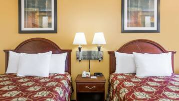 A hotel room with two beds, each with a patterned bedspread, a nightstand with a lamp, and a wall-mounted telephone.