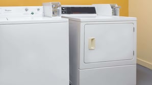 A front-loading Whirlpool washer and dryer stacked side by side in a laundry room with a yellow wall and grey floor.