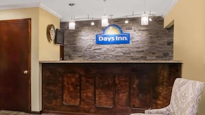 A reception area with a Days Inn sign, a wooden door, a clock, and a patterned armchair.