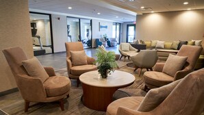 A lobby with multiple seating areas, including sofas and armchairs, arranged around a central coffee table. - Courtyard By Marriott Bentonville (Bentonville)