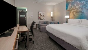 A hotel room with a bed, a desk with a computer, a chair, a couch, and a painting on the wall. - Courtyard By Marriott Bentonville (Bentonville)