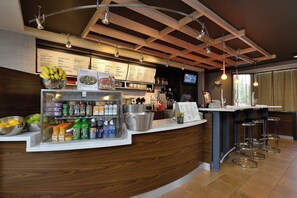 A bar area with a wooden counter, a refrigerated display with beverages, and a menu board. - Courtyard By Marriott Bentonville (Bentonville)