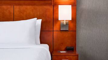 A neatly made bed with white linens, a wooden headboard, a bedside table with a lamp, and a small drawer.