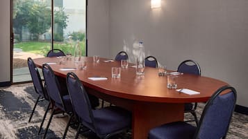 Un salón de conferencias con una mesa de madera, seis sillas y un ventanal de vidrio que da a un jardín.