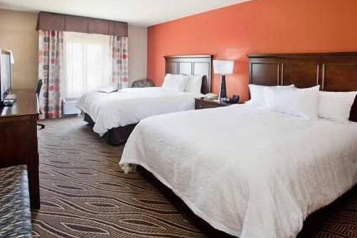 A hotel room with two beds, a desk, a chair, and a window with curtains.