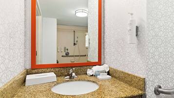 A bathroom with a granite countertop, a white sink, a mirror with an orange frame, and a shower area visible in the background.