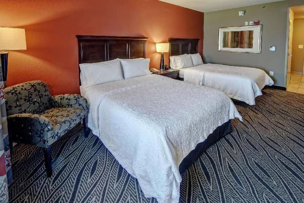 A hotel room with two beds, a sofa, a lamp, and a framed picture on the wall.