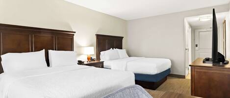 A hotel room with two beds, a desk, a chair, a TV, and a lamp.